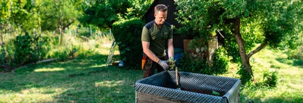 Mann in Arbeitskleidung pflanzt im Hochbeet im Garten bei sonnigem Wetter.